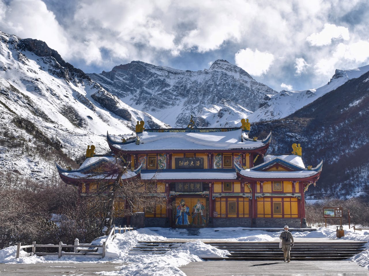A Chinese temple amidst snow-covered mountains under a cloudy winter sky.